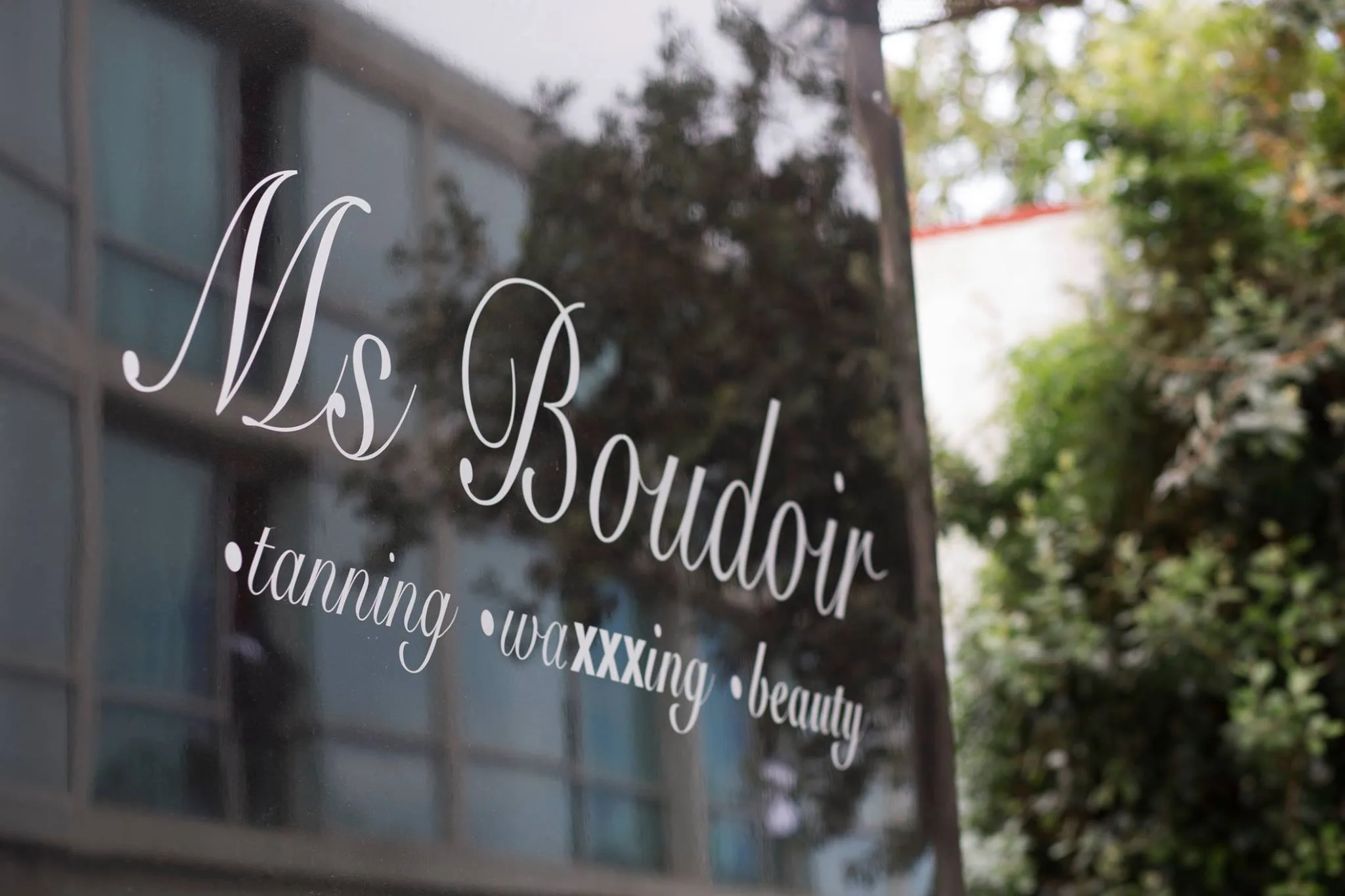 The Ms Boudoir wordmark engraved in fine copperplate on the salon window — Ms Boudoir · tanning · waxxxing · beauty