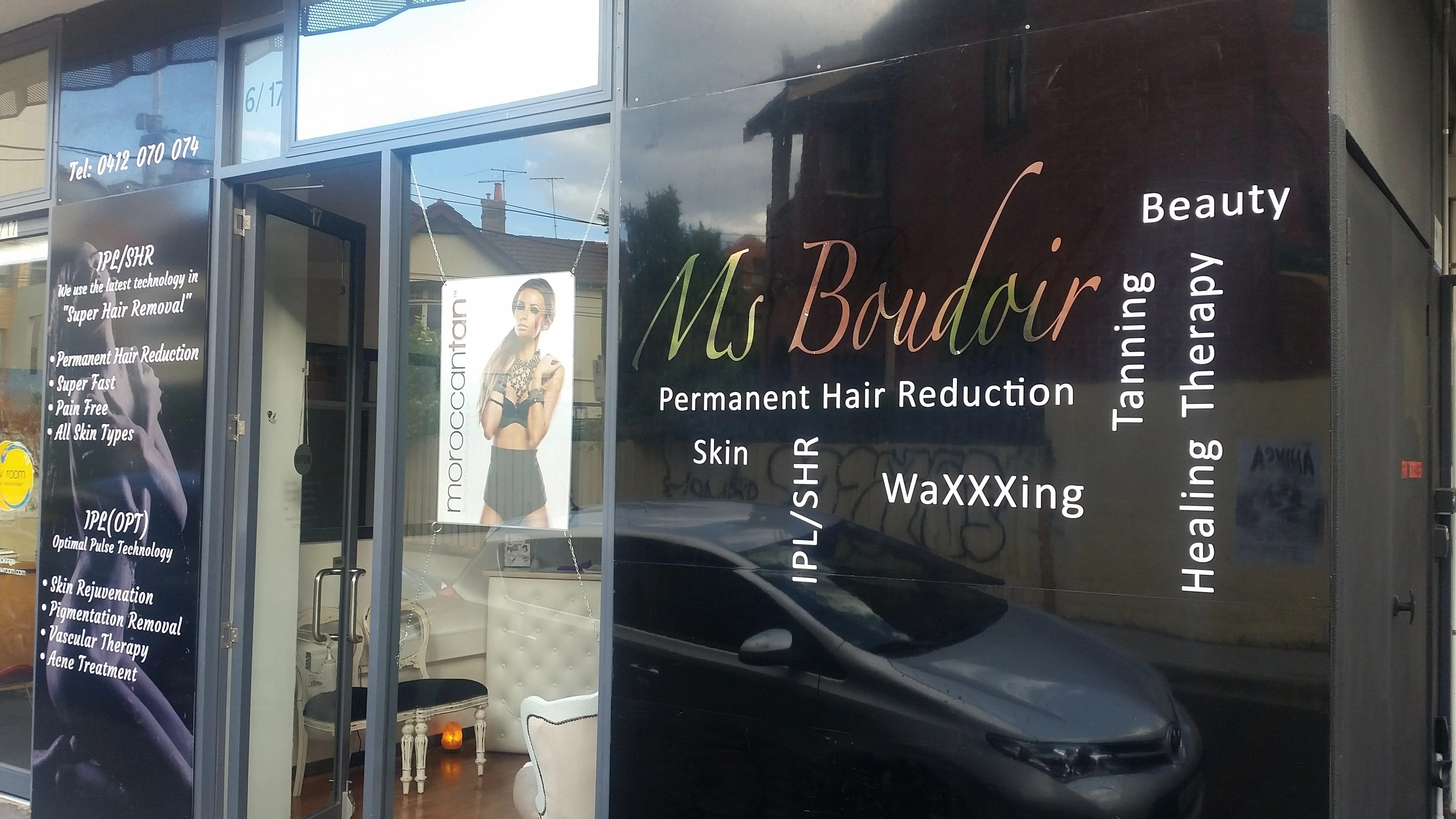 The Ms Boudoir shopfront close — metallic script wordmark with Permanent Hair Reduction, IPL/SHR, WaXXXing, Tanning, Healing Therapy, Beauty on the glazed door; white Queen Anne furniture visible through the open entrance