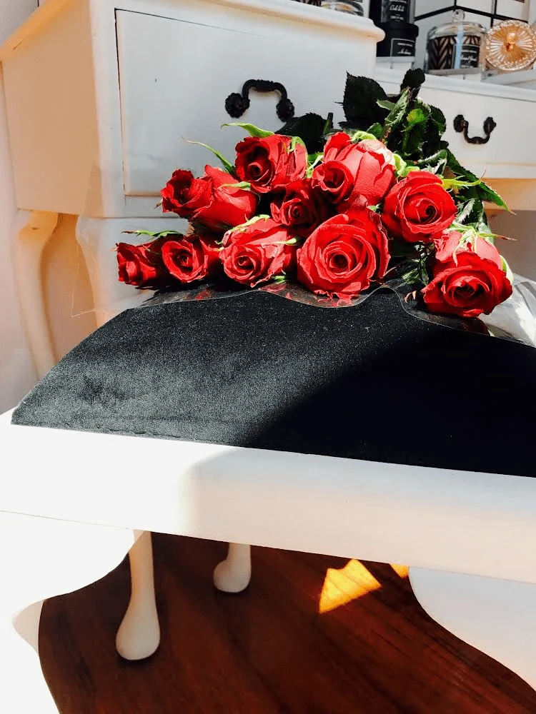 Long-stemmed red roses laid on black velvet across a white Queen Anne console table, with Ms Boudoir black-and-white candle jars on a white dresser behind