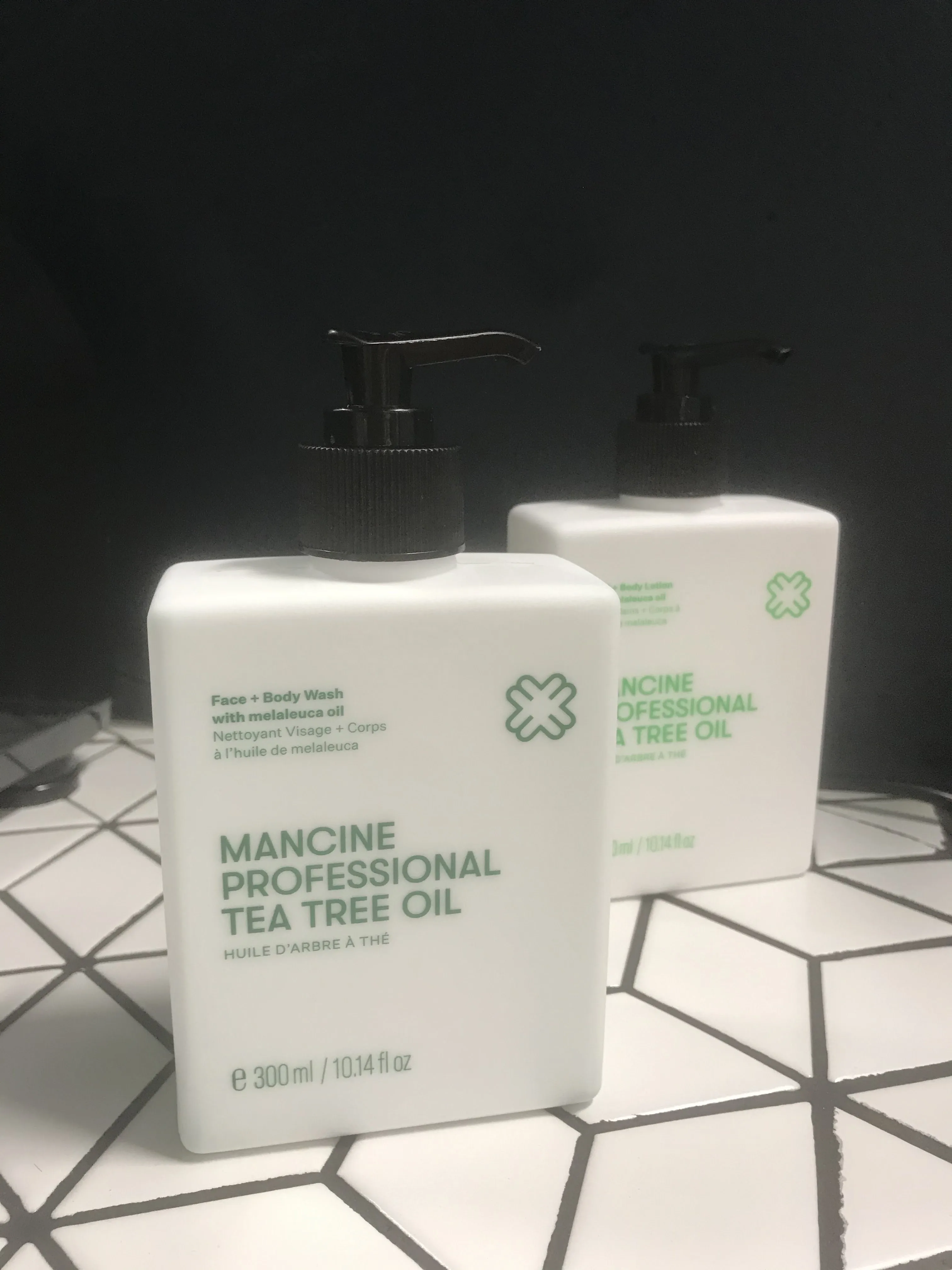 Mancine Professional Tea Tree Oil Face and Body Wash — two pump bottles on the salon's black-tiled bench